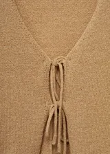 Cárdigan color beige de tejido de punto grueso, con cuello pico, diseño crop, corte recto, cierre de lazo en la parte delantera y manga larga.