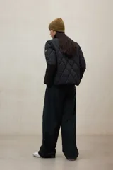 Campera acolchada de color verde militar con diseño de costuras en forma de diamante. Confeccionada en poliéster reciclado, presenta un cuello redondo, cierre frontal con botones a presión y mangas largas. Es una prenda repelente al agua de corte recto.