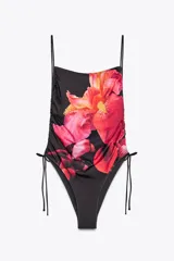 Bañador negro con estampado de flores rojas y amarillas, escote recto, tirantes finos y frunces ajustables con lazadas en los laterales.