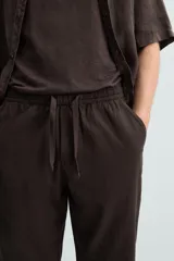 Pantalón de corte relajado (relaxed fit) color verde militar, confeccionado en mezcla de algodón y lino. Presenta cintura elástica ajustable con cordón y bolsillos frontales y traseros de vivo.