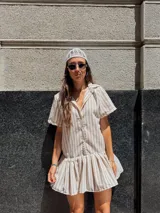 Vestido camisero corto de algodón con rayas verticales color beige y blanco, cuello camisero, cierre frontal con botones y falda con volado.