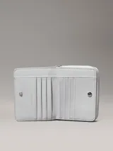 Billetera mediana de color gris claro, con cierre perimetral de cremallera y textura de monograma en relieve. Presenta el logo metálico de Calvin Klein en el frente y tecnología de protección RFID.