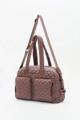 Bolso marrón con diseño matelassé, doble asa corta, correa larga desmontable y dos bolsillos frontales. Incluye llavero de corazón y dijes desmontables.