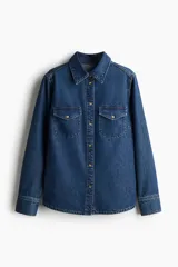 Camisa de denim azul con cuello clásico, cierre frontal con botones a presión, dos bolsillos con solapa abotonada en el pecho, mangas largas con puños abotonados y canesú en la espalda.