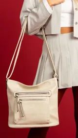 Bandolera beige de símil cuero con dos bolsillos frontales con cierre, un bolsillo trasero, tres bolsillos internos y correa larga regulable.