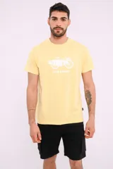 Remera mostaza de algodón con cuello redondo y estampado de una bicicleta con tablas de surf y el texto "Live Simply".