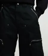 Bermuda negra de estilo baggy, confeccionada en mezcla de poliéster y algodón. Presenta doble trabilla, bolsillos cargo laterales con cremallera y detalles de cremallera visibles.