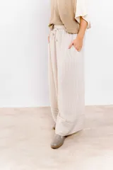 Pantalón de vestir color beige con rayas verticales blancas, corte palazzo, cintura alta con cordón ajustable y bolsillos laterales.