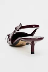 Zapato destalonado color borgoña charol, con tacón kitten y punta fina. Presenta una tira trasera con hebilla ajustable y detalle de hebilla metálica en la parte delantera.
