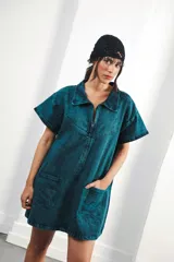 Vestido corto de denim azul con efecto lavado, corte holgado, cuello tipo camisa, cierre frontal con cremallera metálica, bolsillos delanteros y bordados en canesú delantero y trasero.