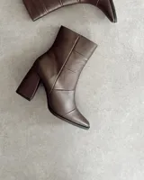 Botín de cuero color marrón con caña media, punta fina y taco geométrico de 10 cm.