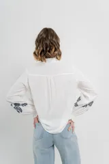 Camisa de manga larga en algodón liviano, color azul marino, con bordados florales en contraste en el frente y mangas. Cuello mao con terminación en ondas y puños fruncidos.