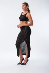 Conjunto de top y falda de tejido de punto calado color negro. El top es corto, de breteles anchos y terminación con flecos. La falda es larga, de tiro alto, corte recto y abertura lateral.