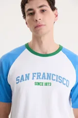 Remera blanca con mangas raglán celestes y cuello verde. Estampado frontal con la leyenda "San Francisco Since 1873" en celeste.