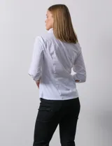 Camisa blanca de algodón con cuello a la base con solapa y escote en V. Abertura central con botones, delantera con detalles plisados y manga ¾ con puño y botón. Laterales en tejido modal.