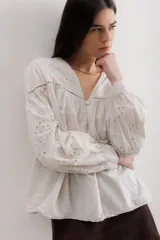 Camisa color crema de algodón con bordado calado, escote en V y mangas largas abullonadas.