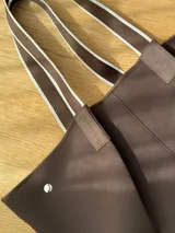 Bolso negro tipo tote de neopreno con bolsillo interno de red, sobre haciendo juego y gancho para sujetarlo.