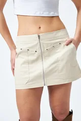 Minifalda color marrón claro, de corte recto con cierre metálico visible al frente y bolsillos decorativos con tachas.