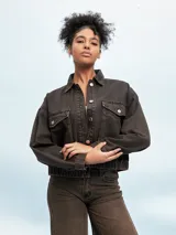 Campera marrón de denim con efecto desgastado, corte cropped, cuello camisero, cierre frontal con botones metálicos, bolsillos con solapa en el pecho y puños abotonados.