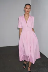 Vestido camisero midi de popelina a rayas verticales rosas y blancas, con cuello solapa, manga corta, bolsillos de parche en el pecho, cinturón de lazo ajustable y cierre frontal con botones.
