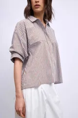 Camisa marrón a rayas verticales blancas y marrones, de corte amplio y mangas cortas.