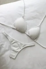 Bikini blanco de lycra texturizada, compuesto por un corpiño de triángulos movibles con tiras finas para atar al cuello y espalda, con almohadillas desmontables, y una bombacha colaless con laterales fijos.