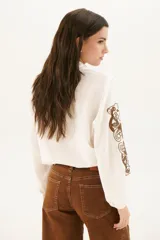 Camisa blanca de manga larga con bordados florales marrones en las mangas.