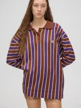 Chomba de corte oversize con cuello camisero, a rayas verticales en color marrón, lila y blanco. Tiene un logo bordado en el pecho y puños en color marrón.