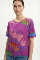 Remera lila con estampado de flores abstractas en tonos rosa, naranja, amarillo y verde.