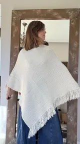 Poncho tejido en lana merino color crudo, con cuello alto y etiqueta de cuero con logo en la espalda.
