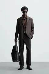 Pantalón de vestir negro de corte recto, confeccionado en tejido de algodón con acabado ligeramente encerado. Cuenta con bolsillos laterales y traseros de vivo. El cierre frontal es con cremallera y gancho metálico oculto.