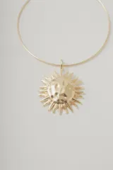 Collar corto dorado con dije grande en forma de sol con detalles plateados.