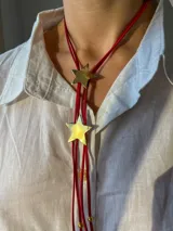 Corbatín rojo de gamuza con dos dijes de estrella dorada.