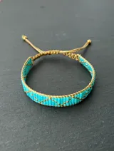 Pulsera tejida con cuentas Miyuki en tonos turquesa y dorado, con cierre ajustable con cordón.