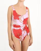Traje de baño enterizo con estampado de flores rojas y hojas color crema sobre fondo lila. Presenta corte alto en la pierna y cinturón lila con lazada lateral.