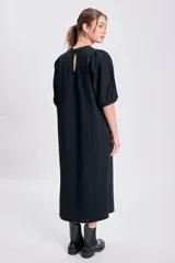 Vestido negro de corte recto y largo midi, con cuello redondo y mangas globo cortas. Presenta pespuntes contrastantes en color claro que recorren el frente y los hombros.