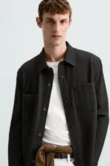 Sobrecamisa negra de tejido con elasticidad, cuello solapa, manga larga con puño abotonado, bolsillos de plastrón en el pecho y cierre frontal con botones a presión.