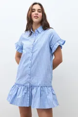 Vestido camisero corto color celeste con rayas blancas y finas rayas rojas. Presenta cuello camisero, botones frontales, mangas cortas con volados y un volado en el ruedo.