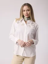 Camisa blanca de algodón con cuello clásico, cierre frontal con botones y mangas largas. Presenta bordados calados con motivos florales en la parte superior.