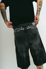 Bermuda de jean negro con lavado ácido gris, corte baggy y bolsillos grandes. Presenta bordados plateados y blancos, cierres y botón personalizado.