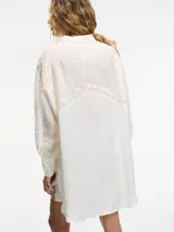 Camisa celeste con bordados blancos, cuello camisero, cierre frontal con botones y mangas largas con puños blancos.