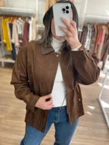 Chaqueta marrón de símil gamuza con cuello de cuerina, cierre frontal, bolsillos con solapa y elástico ajustable en la cintura.