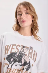 Remera blanca de corte amplio con estampa de un cowboy montando un caballo y la frase "Western Cowboy" en letras marrones y estilo cuerda. 