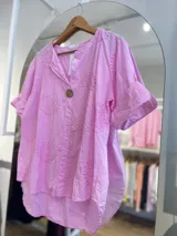 Blusa color crema con cuello camisero, mangas cortas con dobladillo y cierre frontal con un botón de madera. Presenta bordados con motivos de paisley y perforaciones.