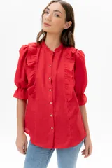 Blusa de lino color rojo con volados frontales que enmarcan el pecho, cuello redondo con mini volado y mangas 3/4 abullonadas con puño elástico. Presenta un cierre frontal con botones y una silueta relajada.