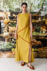 Vestido largo de lino color crudo con cuello semi-bote y tajos laterales. Presenta vivos de color fucsia que delinean el escote, sisas y recorren el cuerpo en líneas diagonales asimétricas.