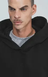 Hoodie negro de corte oversize con capucha, bolsillo tipo canguro y detalle de bolsillo con cierre en la manga izquierda.