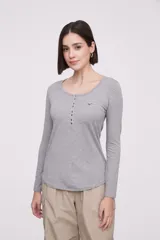 Remera de manga larga entallada en color blanco, confeccionada en algodón. Presenta cuello redondo con una hilera de botones frontales y un pequeño bolsillo en el pecho con detalle de botón.