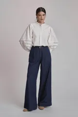 Camisa blanca de mangas largas abullonadas con detalles de calado en los puños, cuello mao y cierre frontal con botones.