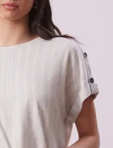 Blusa de lino color blanco con rayas verticales, de la marca Cable & Gauge. Tiene hombros con aplique de botones.